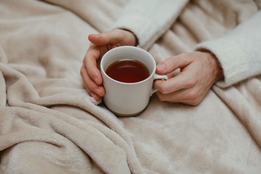 Hands holding a warm mug of tea on a soft blanket