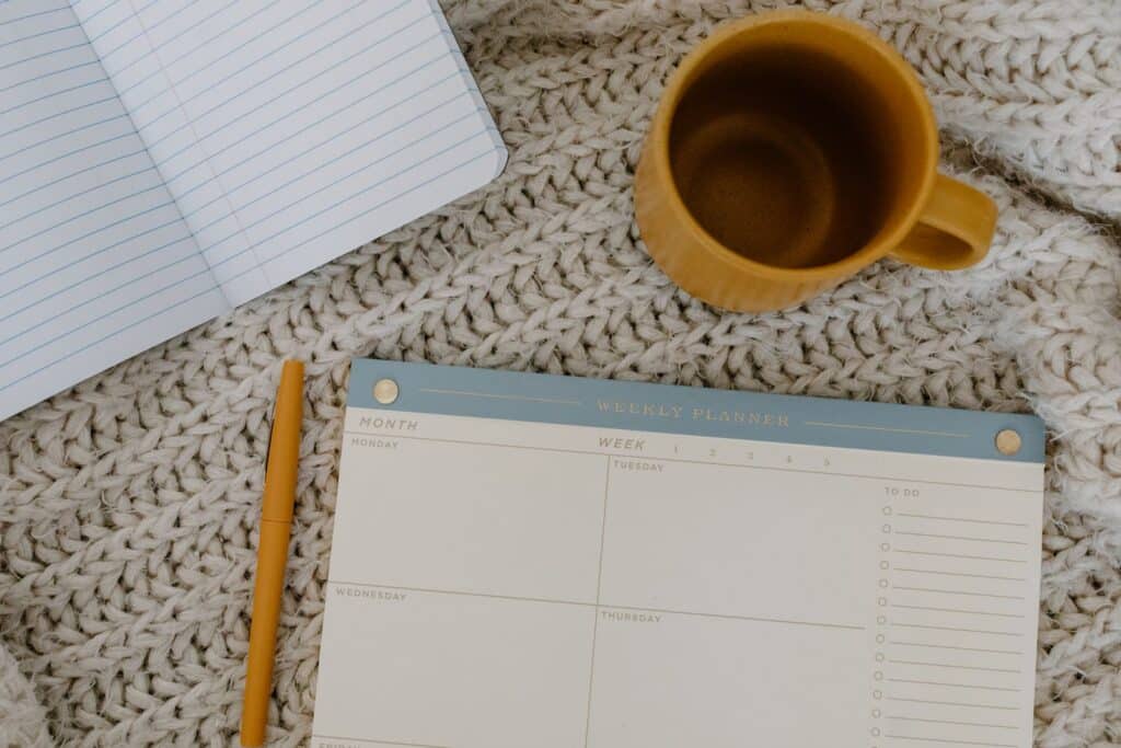 Weekly planner, notebook, and coffee on a cozy knit blanket